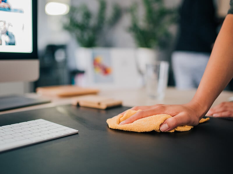 Person cleaning desk with cloth in office