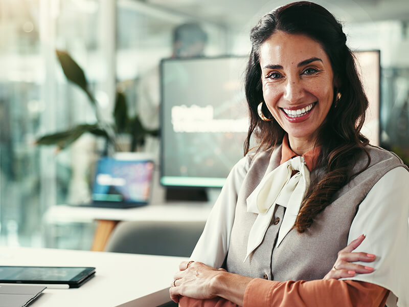 Smiling woman in office environment, arms folded.
