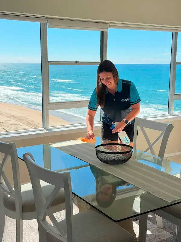 Professional cleaner wiping glass dining table in beachfront apartment